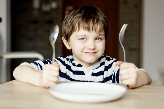 child at table with spoon and fork