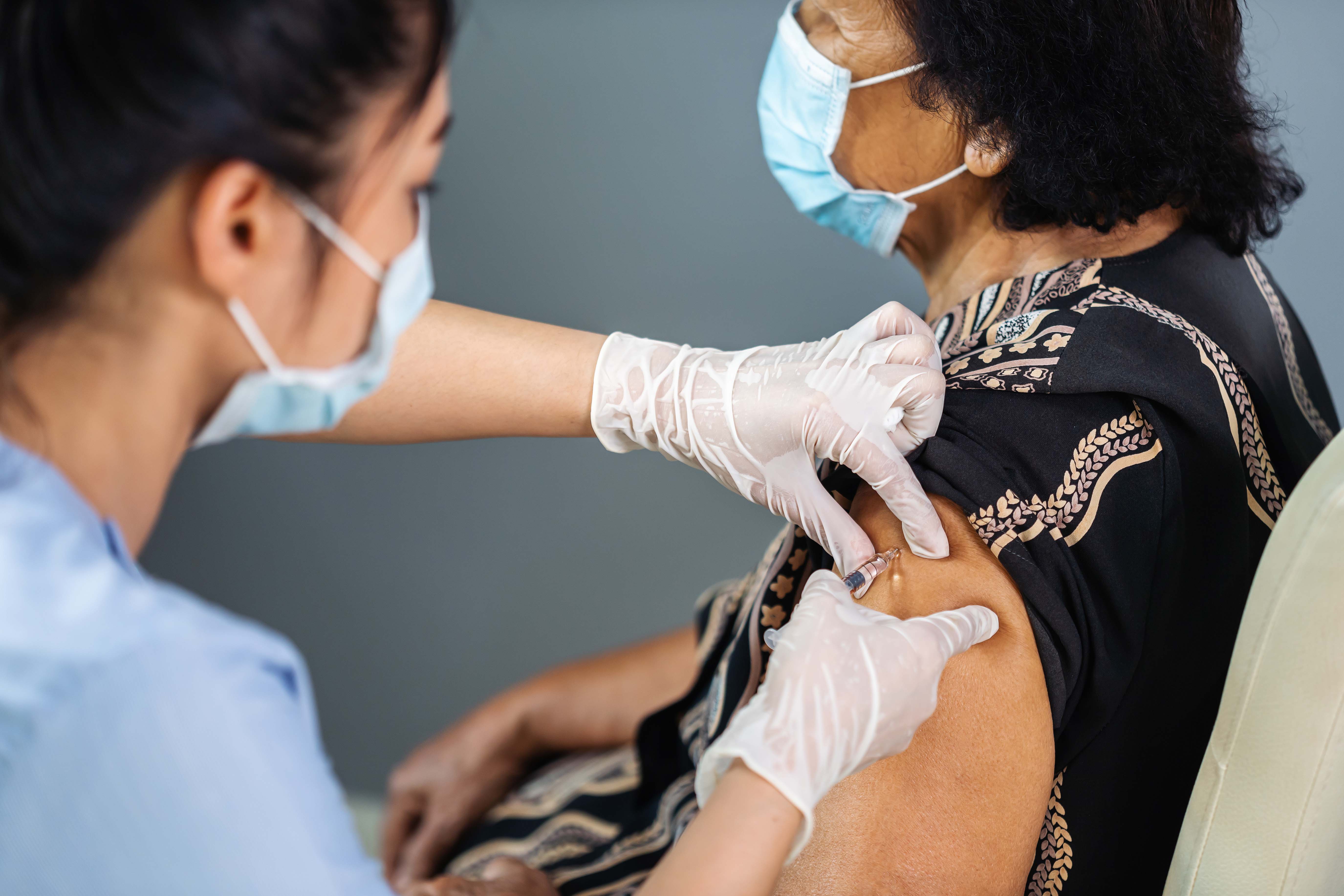 Nurse with mask giving vaccine to elderly woman with mask