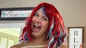 A woman wearing a red wig and a goofy grin