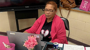 a woman in a hot pink blazer sits at a laptop