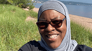 A woman wearing sunglasses and a hijab smiles in the sunshine